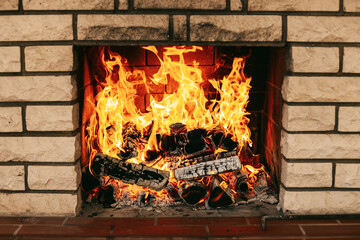 A warm, roaring fire in a fireplace embedded in a light brick wall, featuring vivid orange and yellow flames consuming dark logs