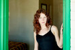 © Connect Images - A woman with curly red hair stands in a doorway, wearing a black tank top and giving a focused look.
