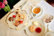 © Connect Images - An elegant afternoon tea setup featuring a selection of cakes, a teacup, and a teapot on a table, accented by a vase with pink tulips.