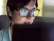 © Connect Images - A focused individual wearing glasses with computer code reflection in the lenses is intently looking at a computer screen.