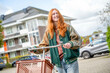 © Connect Images - A smiling young woman with red hair is pushing a shopping cart outdoors on a sunny day. She is dressed in casual clothes with a green jacket and blue jeans.