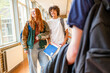 © Connect Images - Two students are walking down a school hallway, smiling and engaging in conversation, with books in hand.