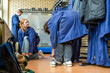 © Connect Images - Workers in protective overalls are in a locker room, with one squatting and another standing amidst lockers and hanging work garments.