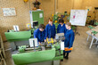 © Connect Images - Four individuals in blue work attire are operating green industrial machinery in a workshop setting, collaborating on a technical task.