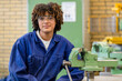 © Connect Images - A person in safety glasses and blue work overalls is sitting in a workshop, smiling at the camera with industrial equipment in the background.