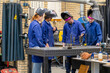 © Connect Images - Four people dressed in protective work gear, including welding helmets, are engaging in a welding activity at a workshop table equipped with metalworking tools.