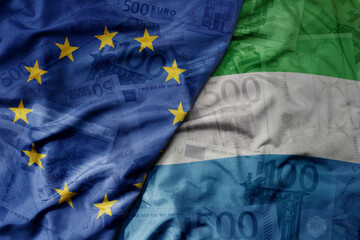 big waving realistic national colorful flag of european union and national flag of sierra leone on a euro money banknotes background.