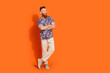 © deagreez - Full size photo of positive man wear stylish shirt white pants arms crossed look at sale empty space isolated on orange color background