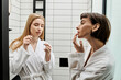 © Bliss - A young woman in a bathrobe flossing her teeth while looking at her partner in a hotel bathroom.
