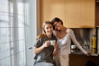 © Bliss - Two women, a young lesbian couple, share a cozy moment while standing in a hotel kitchen with coffee in hand.