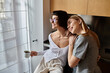 © Bliss - Two young women, a lesbian couple, standing close with coffee inside a hotel room kitchen.