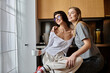© Bliss - A young lesbian couple sitting closely, chatting over coffee in a cozy hotel kitchen.