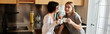 © Bliss - A young lesbian couple chat over coffee cups, standing together in a cozy hotel kitchen.