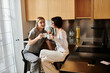 © Bliss - A young lesbian couple enjoying coffee together on a kitchen counter inside a hotel room.