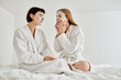 © Bliss - A beautiful lesbian couple in sheet masks and bath robes peacefully sitting on a luxurious hotel bed together.