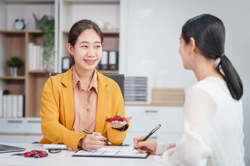 Asian businesswoman and a salesman discuss car sales, insurance, and financing with a customer at a desk, covering used car loans, premiums, deductibles, and various insurance coverage options.