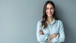© Creations Photo  - Happy young smiling confident professional business woman wearing blue shirt, pretty stylish female executive looking at camera, standing arms crossed isolated at gray background.