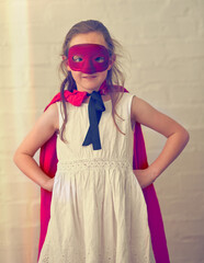 Child, girl and portrait of superhero on wall background for game, playing or fantasy for power. Confident kid, mask and cape costume for pretend, dream and hero cosplay to fight for justice by brick