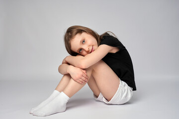 full length portrait of a cute girl, wearing white shorts and black shirt, sitting on white backgrou