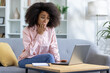 © Liubomir - Worried woman with laptop sitting on a couch at home, looking shocked and concerned as she reads online news or email.