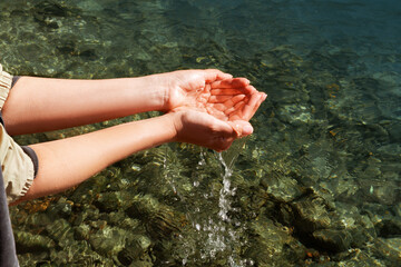 A woman touches the water with her hands. Women's hands collect water in their hands near the river, sea, ocean. Happy. People in nature.