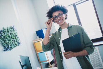 Poster - Photo of happy positive broker wear khaki shirt spectacles holding clipboard preparing contract indoors workshop workstation