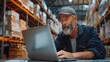 © เลิศลักษณ์ ทิพชัย - A senior male entrepreneur in a mail delivery warehouse uses his laptop to confirm an online drop shipping logistics businesses e-commerce package order.