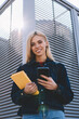 © BullRun - Half length portrait of pretty smiling blonde blogger sending funny messages to friends via modern smartphone.Gorgeous happy teenager looking at camera while installing application on telephone