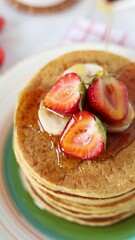 Wall Mural - Pouring maple syrup on pancakes with fresh strawberries and banana for breakfast. Top view. Vertical video. Close-up.