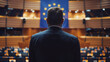 © mila103 - A man in a suit stands in front of a large flag