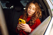 © maxbelchenko - Young beautiful woman passenger uses a smartphone sitting on car. Concept of technology, traveling by car, business.