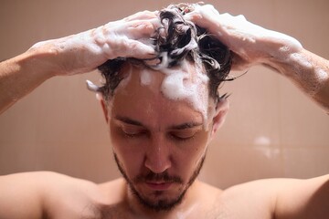 Man washing hair with shampoo in shower, creating foamy lather - personal hygiene care.