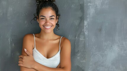 Wall Mural - Portrait of a young latin woman with pleasant smile and crossed arms isolated on grey wall with copy space. 