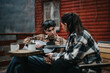 © qunica.com - Two young adults engaged in a relaxed conversation outdoors, with a guitar and coffee on a table, by a wooden cabin.