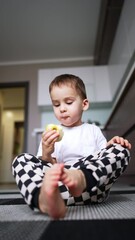 Poster - Calm peaceful baby boy sitting on the kitchen floor. Kid eating healthy tasty apple. Low angle view. Vertical video.