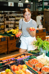 Wall Mural - Young woman shopper choosing tomatoes in grocery store