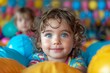 © LifeMedia - Smiling boy with curly locks playing in a colorful ball pit looking at the camera