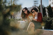 © qunica.com - Two professional businesswomen holding a meeting outside, with documents and digital tablet on a bright day.