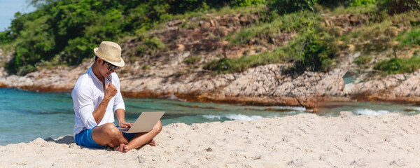 Wall Mural - Banner Man traveler use laptop on summer beach blue sky. Asian man travel relax sitting summer beach island. Man typing laptop computer holiday business trip freelance working online with copy space