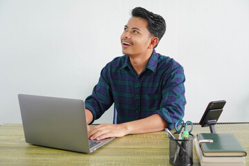 pensive young asian man in blue shirt sit work at wooden desk with pc laptop isolated on white backg