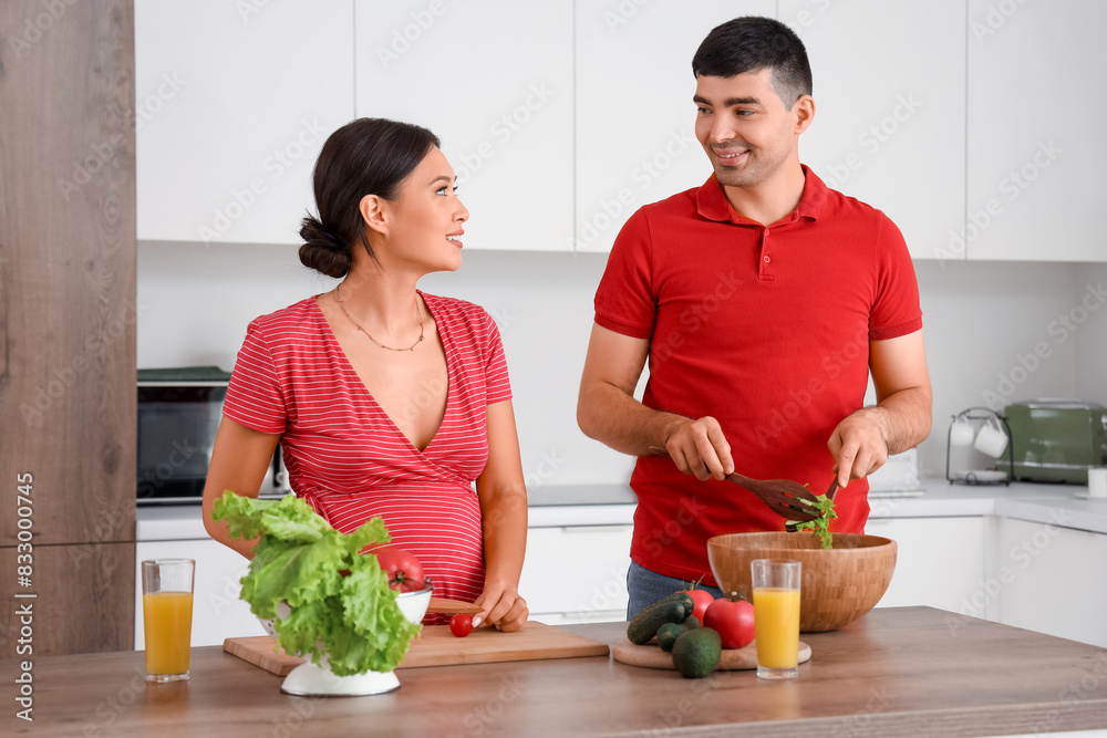 Happy young pregnant couple cooking in kitchen