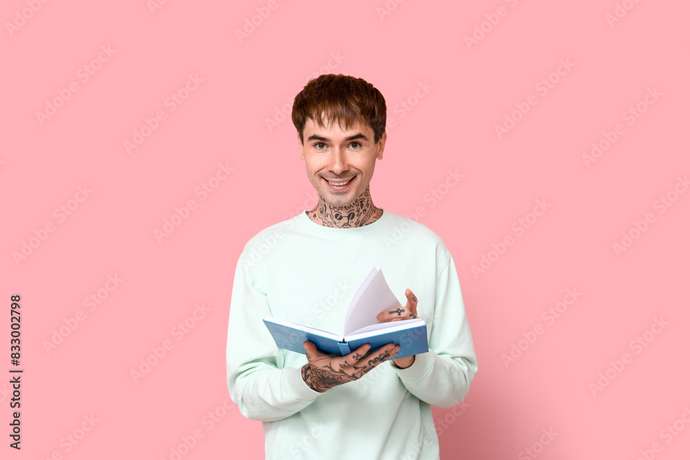 Young tattooed man with book on pink background