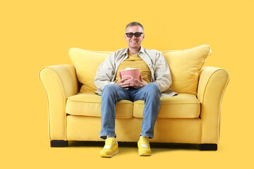 Sticker - Mature man in 3D glasses with popcorn on sofa watching movie on yellow background