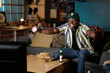 © AnnaStills - Medium long shot of cheerful African American baseball fan watching match on TV late in evening, copy space