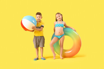 Wall Mural - Cute little children with beach ball and inflatable ring on yellow background