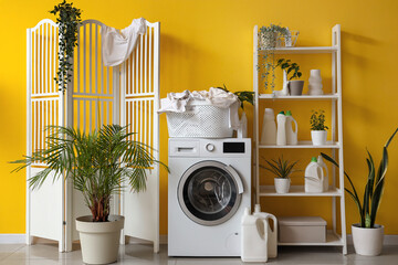 Sticker - Modern washing machine with laundry and bottles of detergent near yellow wall