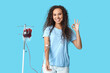 © Pixel-Shot - Young female African-American donor with applied medical patch donating blood and showing showing OK gesture on blue background