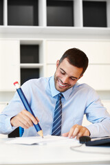 Wall Mural - Office, smile and businessman with big pencil by desk for corporate finance, planning and notes. Happy, man and writing on paper at workplace for investment, budget idea and research of economy