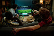 © AnnaStills - Rear view of four young male friends spending evening indoors watching soccer match on TV and drinking beer