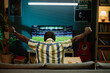 © AnnaStills - Back view of unrecognizable young Black man sitting on sofa in living room enjoying watching football match on TV